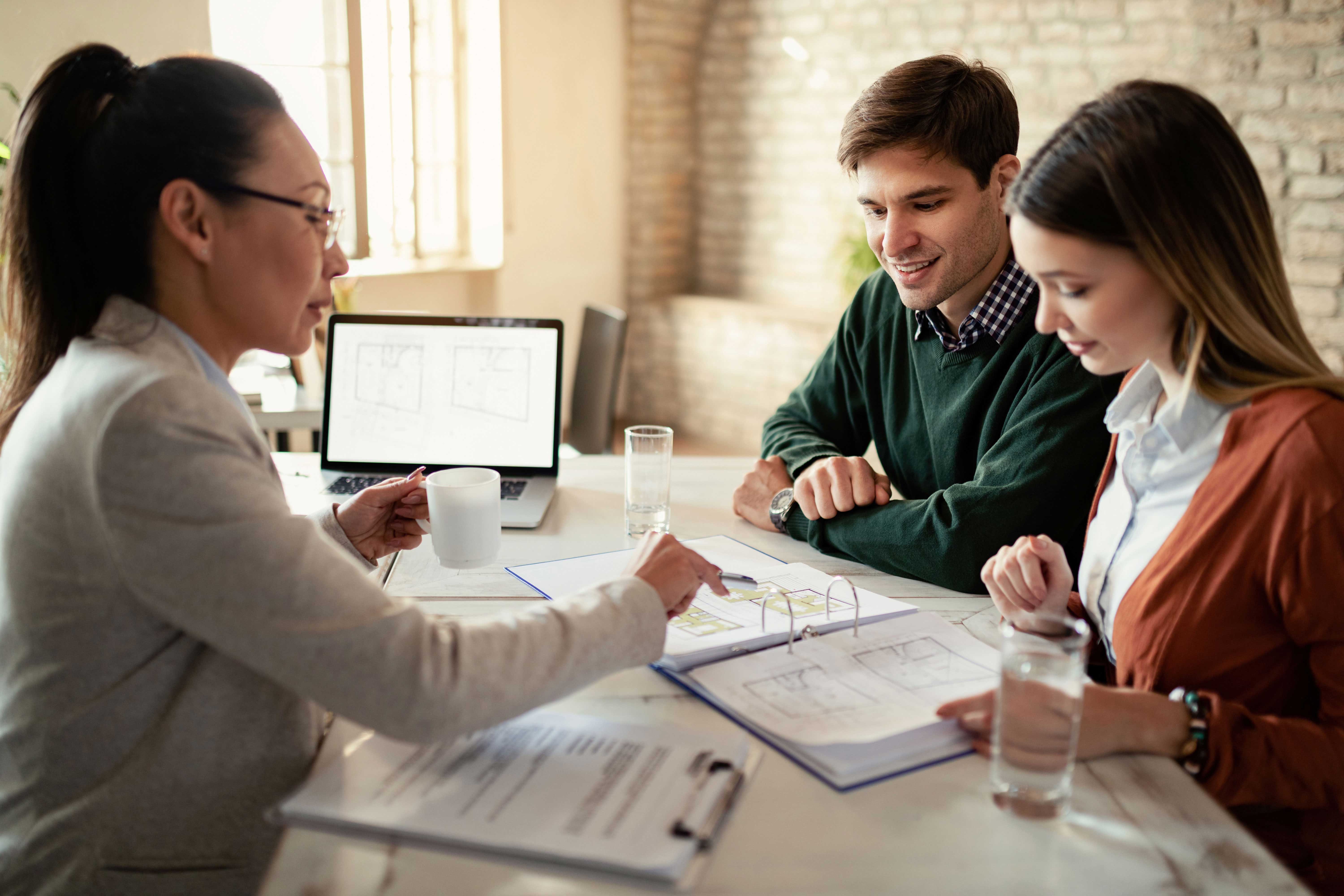 smiling-couple-insurance-agent-going-through-real-estate-plans-during-meeting-office-focus-is-man2